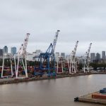 Contêineres e guindastes em um porto de Buenos Aires, com o horizonte da cidade ao fundo