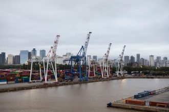 Contêineres e guindastes em um porto de Buenos Aires, com o horizonte da cidade ao fundo